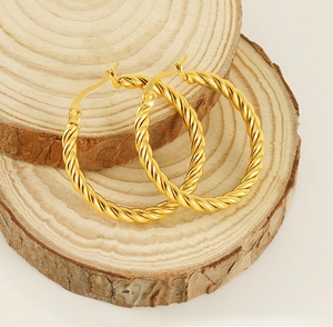 Detailed close-up of golden twisted rope hoop earrings on natural wood blocks