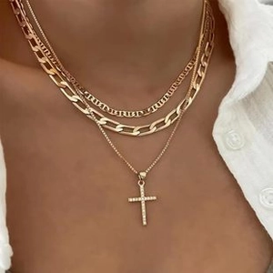 Detail of layered gold necklaces with Figaro chain and diamond-studded cross pendant