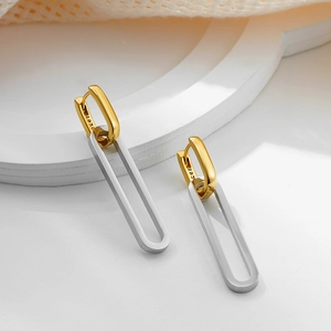 Two-tone 18K gold and silver stainless steel dangling earrings on white geometric props