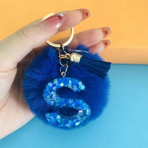 Blue pompom keychain with resin letter S pendant and tassel held against a split background