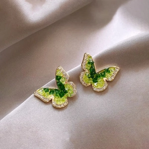 Close-up of golden butterfly stud earrings with green stones and sparkling zirconias