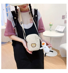 Detail of a beige corduroy crossbody bag featuring a cute bear patch and duck plush charm