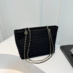 Chic black tote bag with woven texture and gold chain leather strap on white surface