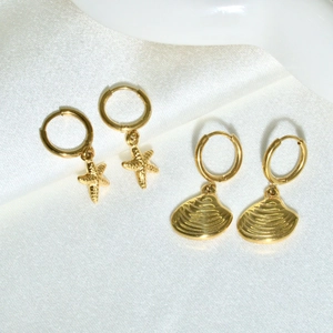Detailed view of 14K gold plated starfish and shell dangle hoop earrings on white silk
