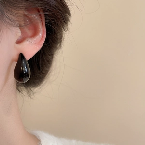 Close-up of a minimalist black teardrop earring with a glossy finish on a female model