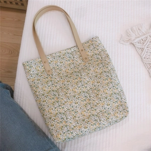 Top view of yellow floral canvas tote bag with leather straps on soft bedding
