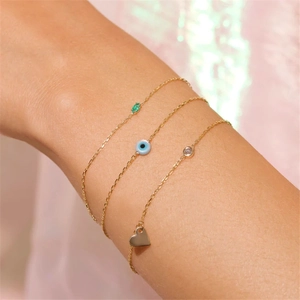 Close-up of a delicate gold evil eye bracelet set with green gems and heart pendant