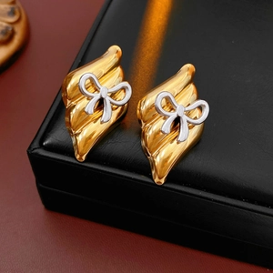 Close-up of gold wavy earrings with silver bow accents on a black leather jewelry box