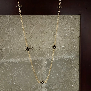Detail of gold necklace featuring five black clover motifs on vintage glass background