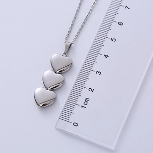 Detailed close-up of a triple heart pendant necklace in silver with a metric ruler scale