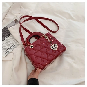 Close-up of a stylish red heart-quilted patent leather handbag with a heart charm