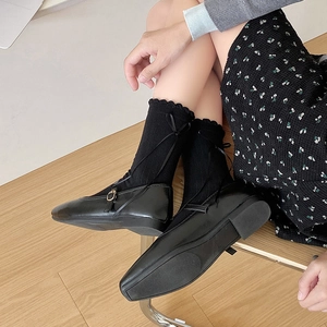 Close-up of black Mary Jane shoes styled with bow-tie lace socks on light wood floor