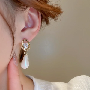 Close-up of vintage gold earring with irregular frame, zircon and baroque pearl