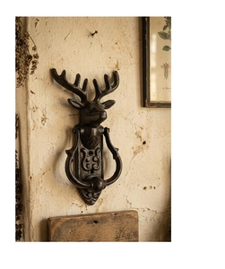 Detailed close-up of a rustic cast iron deer head door knocker on a textured wall
