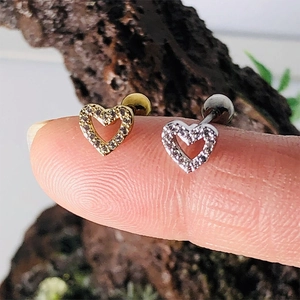 Detail view of gold and silver heart stud earrings with zircons held on a fingertip