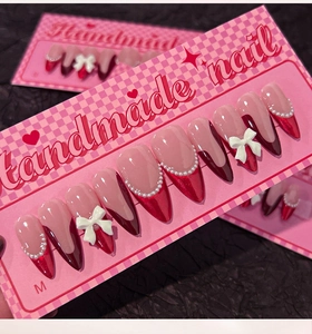Detail of red French press-on nails with 3D white bows and elegant pearl chains