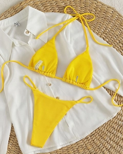 Flat lay of bright yellow ribbed halter bikini set on straw mat for summer vacation