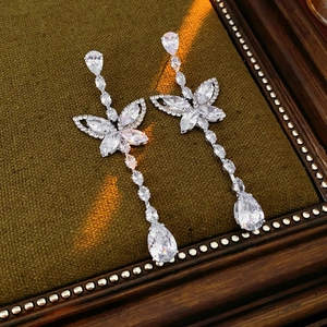 Detail of silver butterfly earrings with pear-shaped cubic zirconia drops on green fabric