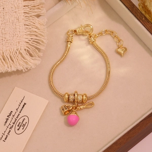 Golden snake chain bracelet with pink tulip pendants and a bow charm on a display tray