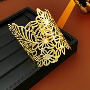 Close-up of golden hollow cuff bracelet with intricate floral and leaf pattern details