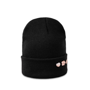 Close-up of black knit beanie featuring decorative pink heart and flower embellishments