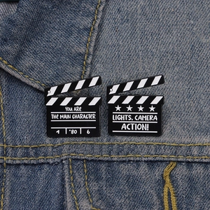 Creative film clapperboard enamel brooches in black and white on blue denim background