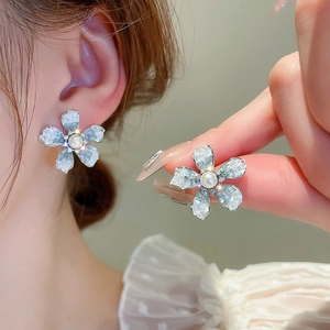 Detail of blue petal flower stud earrings with white pearl center on model