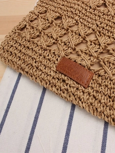 Handwoven straw crossbody bag with brown leather label on natural wood background