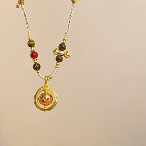Detail of tiger eye stone and red agate beads on a gold hollow pendant necklace