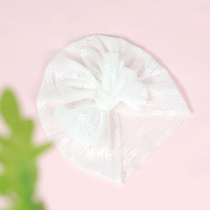 Detail of white lace newborn turban hat with a large decorative floral bow on pink background