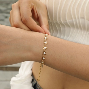 Close-up of golden heart-shaped enamel bracelet worn on wrist with adjustable chain