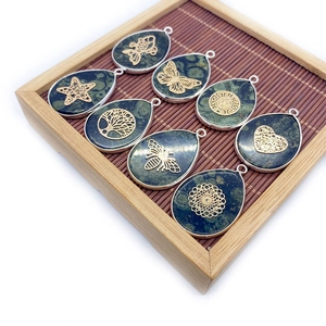Eight teardrop gemstone pendants with golden metal tree and animal motifs in a bamboo tray