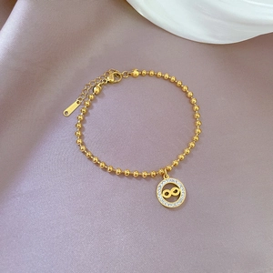Detail of gold-plated stainless steel infinity charm bracelet with zircon on purple satin