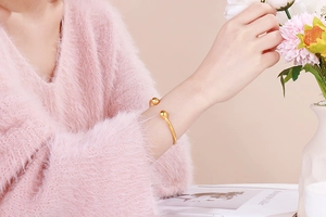 Close-up of golden minimalist open cuff bracelet with spherical ends worn on a wrist