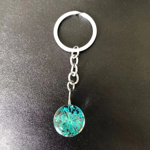 Detail of silver keychain with round glass pendant featuring real blue dried flowers inside