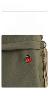 Detail of strawberry cat enamel pins displayed on a green canvas bag with styling icons