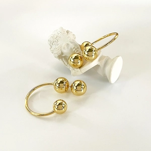 Minimalist golden triple sphere stud earrings on a classic white plaster sculpture