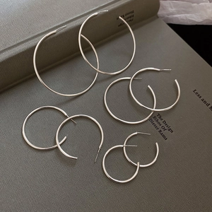 Flat lay of four pairs of silver C-shaped geometric hoop earrings on a vintage book