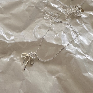 Detailed view of silver bow pendant necklace on textured background with soft lighting