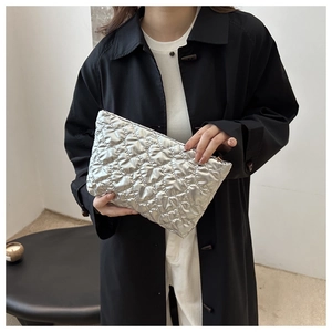 Close-up of a silver quilted heart pattern clutch bag held by a model in a black coat