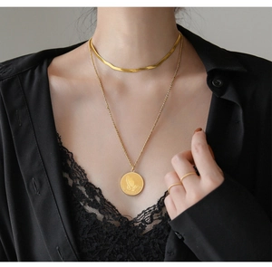 Detailed view of layered gold snake chain and coin pendant with Praying Hands engraving
