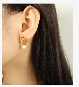 Close-up of golden wing-shaped earring with a white pearl drop on model