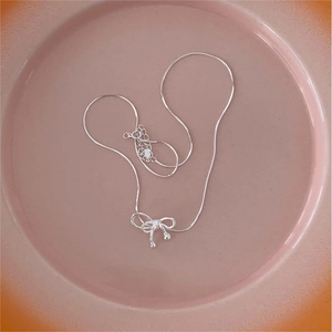 Detail of 925 sterling silver bow pendant necklace with snake chain on pink ceramic dish