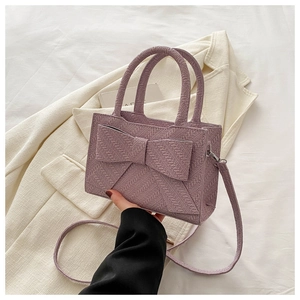 Close-up of lavender woven handbag featuring a large bow detail and round top handles