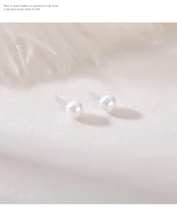 Macro detail of elegant round pearl earrings with silver posts on a soft white feather