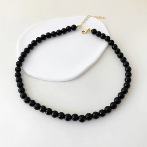 Close-up of black onyx bead necklace with a refined gold clasp on a white surface