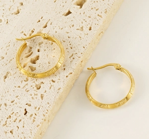 Detailed shot of gold hoop earrings with Greek key pattern on beige stone base