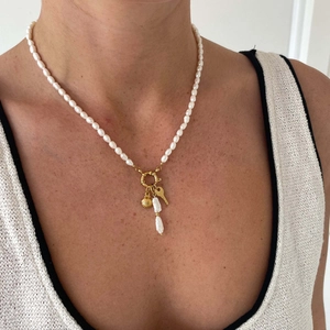 Detail of pearl necklace with gold spring clasp, shell and key charms on a model