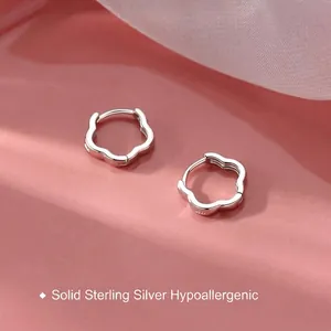 Hollow flower petal sterling silver hoop earrings with elegant wavy design on pink background