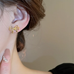 Close-up of elegant golden bow stud earrings on model showing polished metallic texture